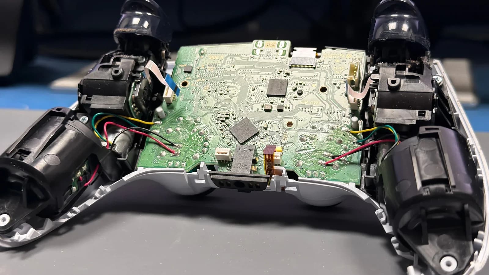 Rozebraný ovladač DualSense s odkrytou deskou a motory vibrací